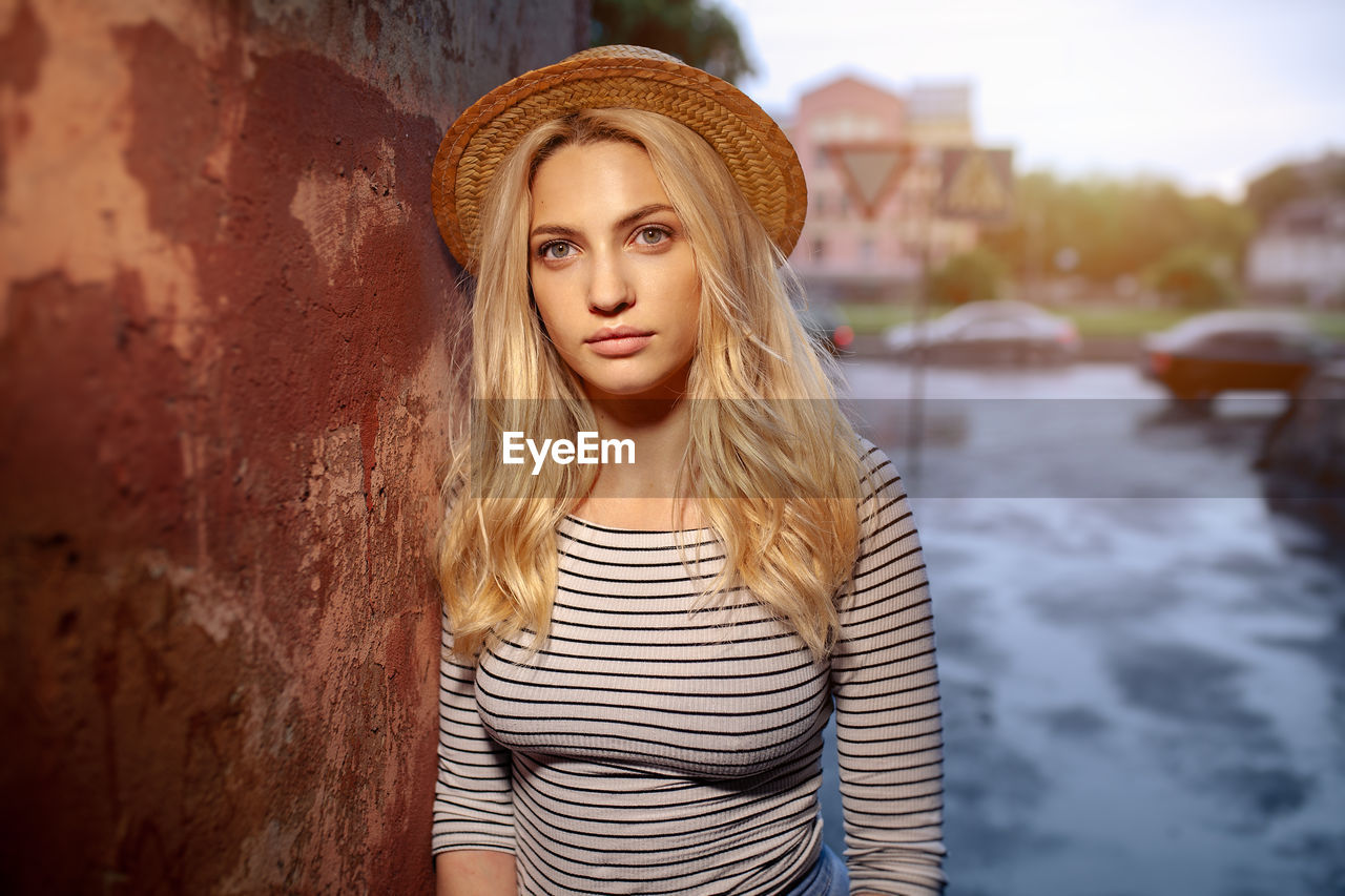 Portrait of beautiful young woman standing by wall