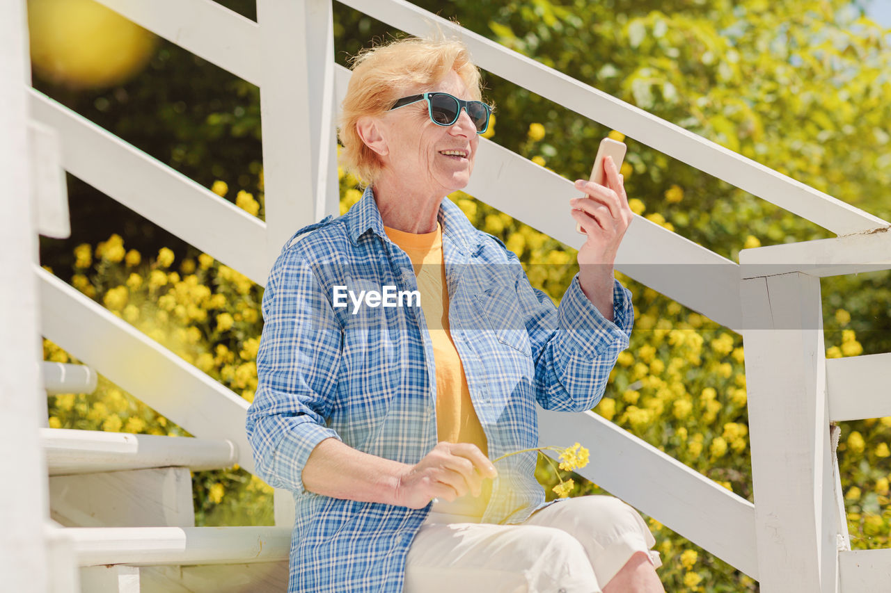 Mature woman sitting alone on the terrace of beach cafe and using mobile phone