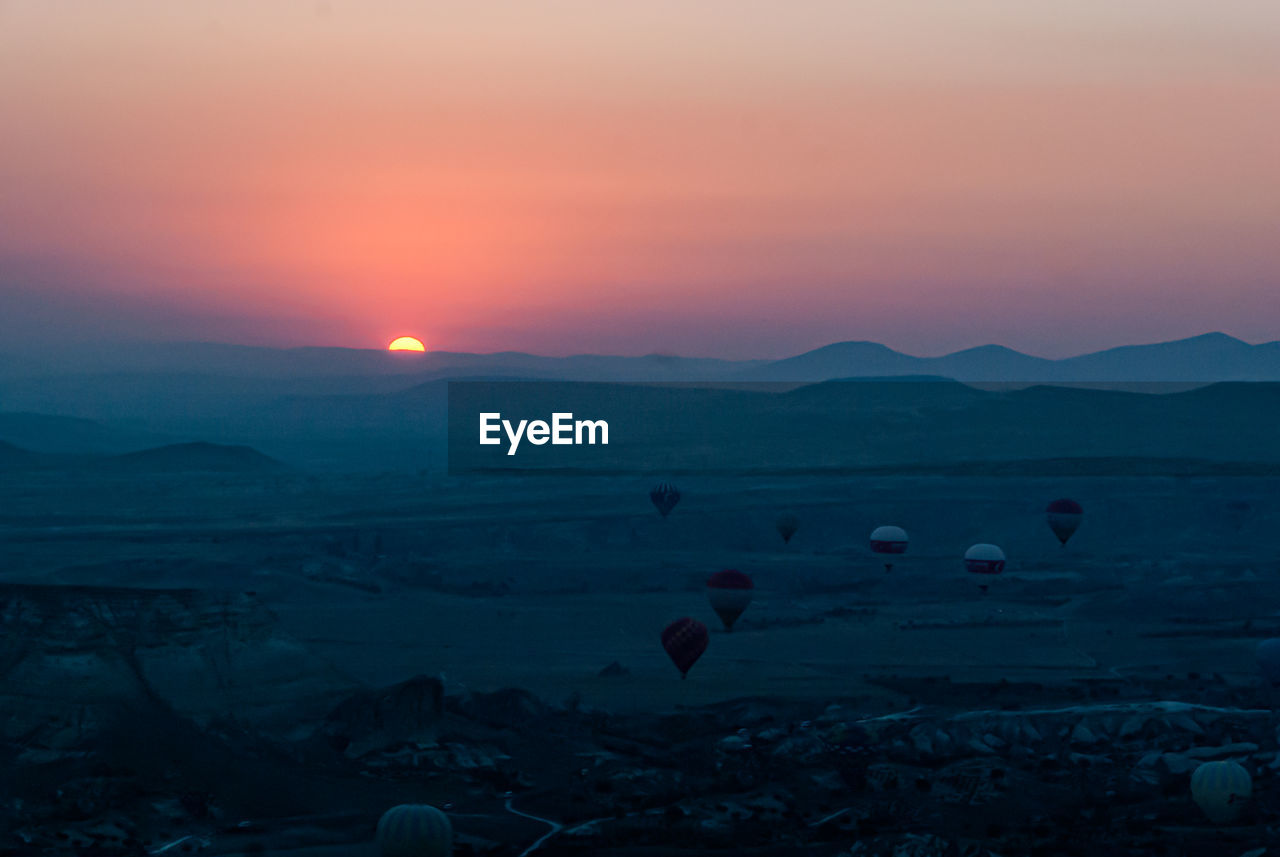 Scenic view of hot air balloons flying over landscape during sunset