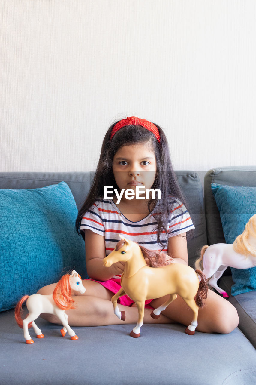 Portrait of cute girl sitting on sofa with dog at home