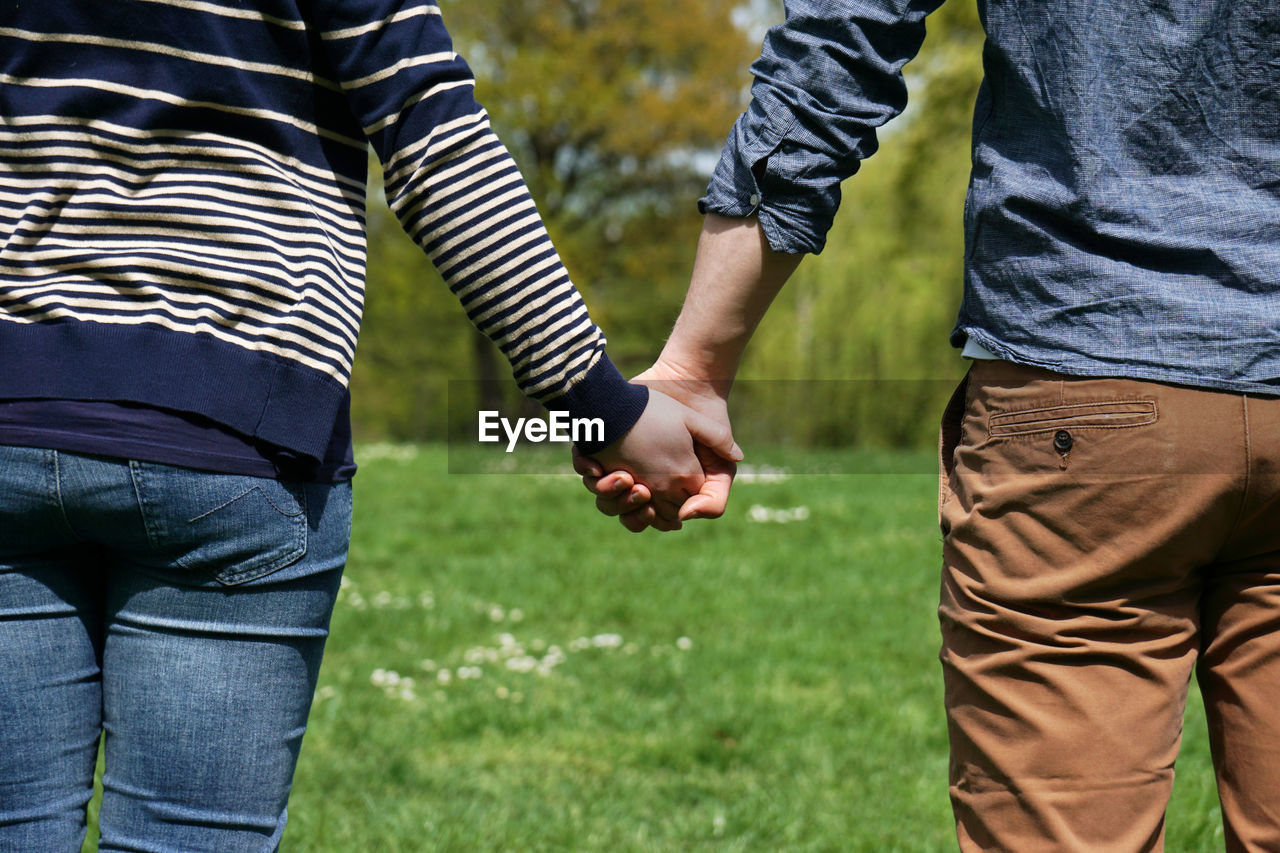 Midsection of couple holding hands at park