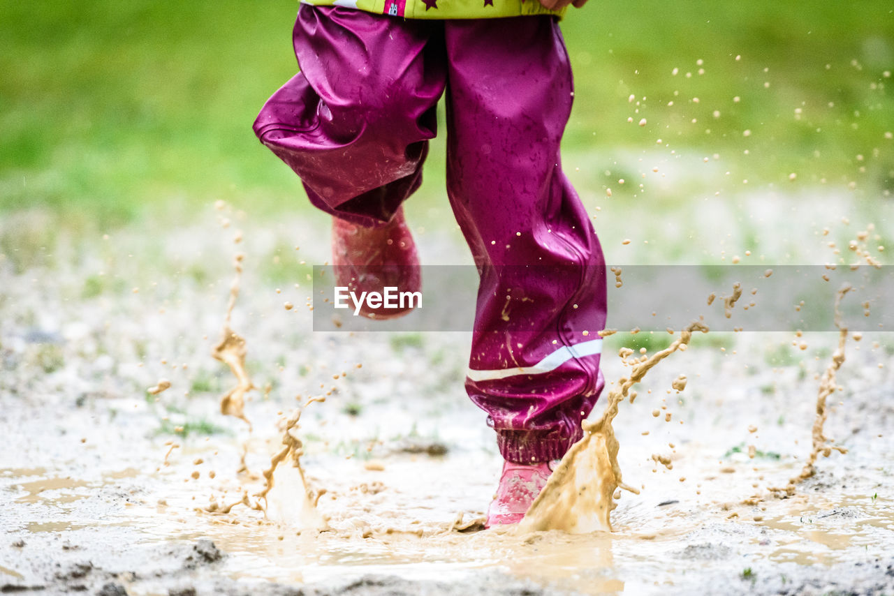 Low section of child playing in puddle on field