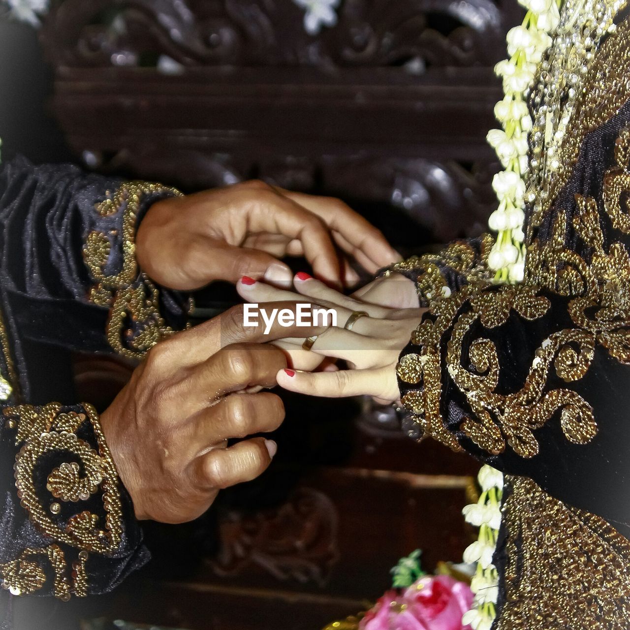 Midsection of bridegroom putting ring on woman finger in wedding ceremony