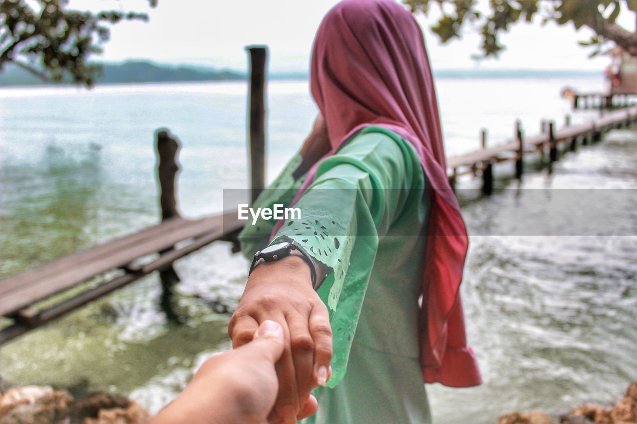 Cropped image of man holding woman hand by lake