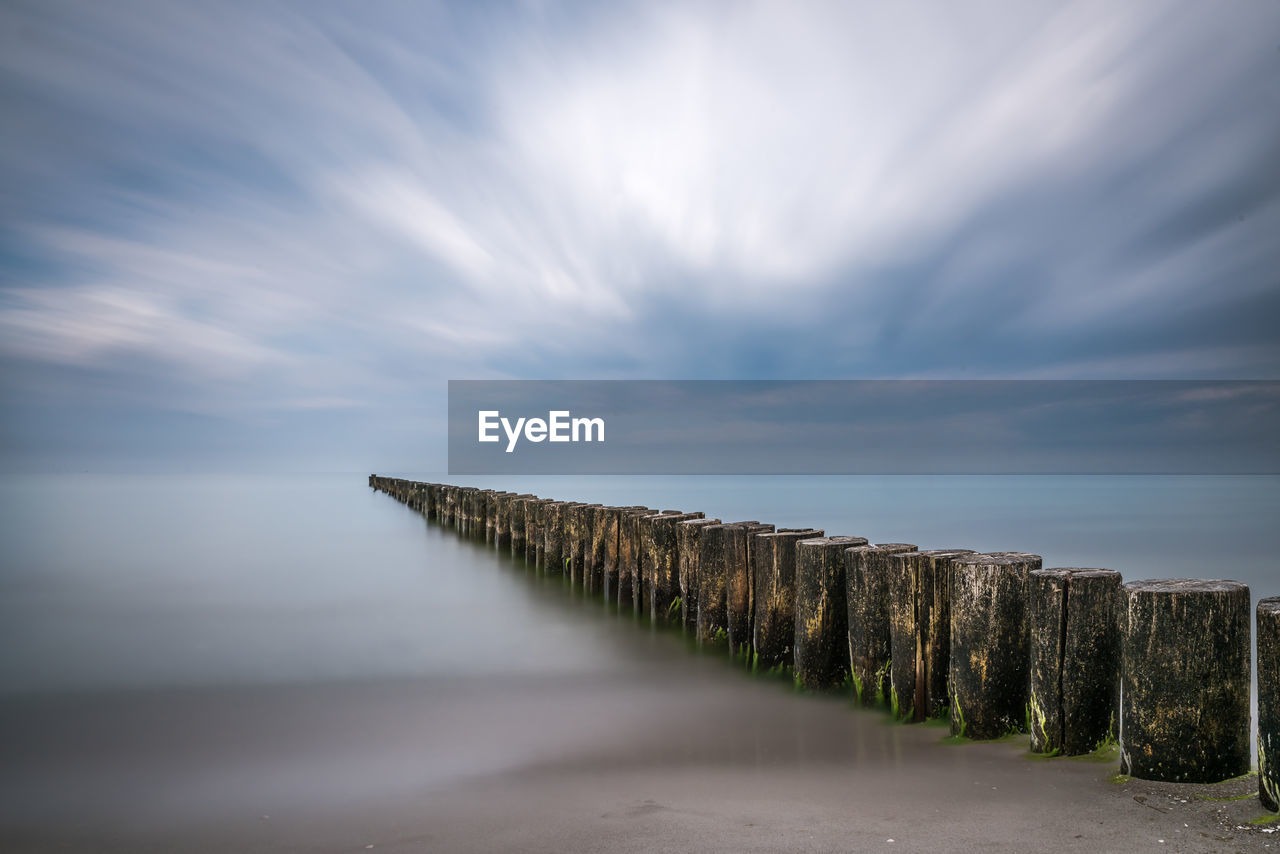 Wooden groyne in lake against cloudy sky