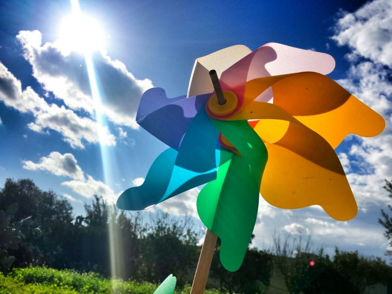 Low angle view of pinwheel against cloudy sky on sunny day