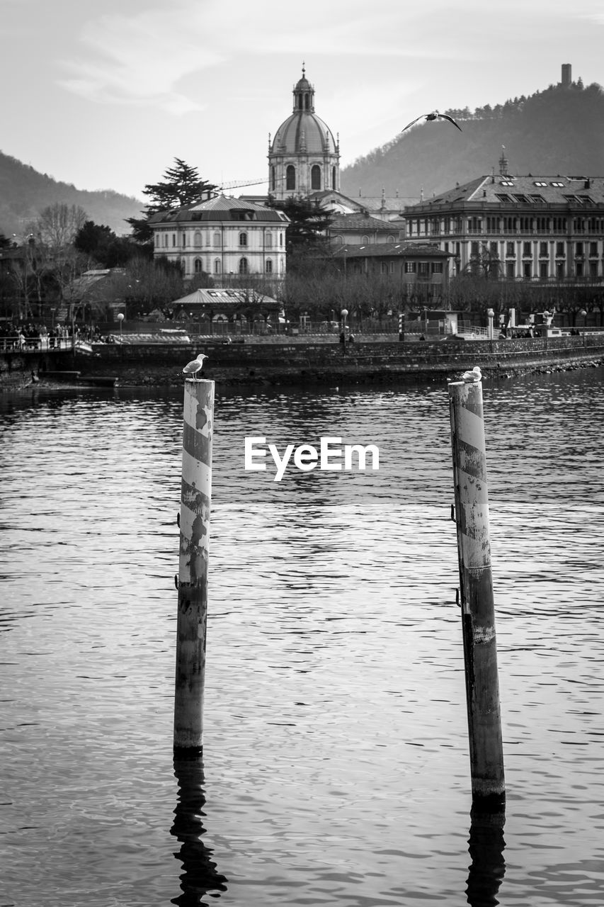 WOODEN POST IN RIVER BY BUILDING AGAINST SKY