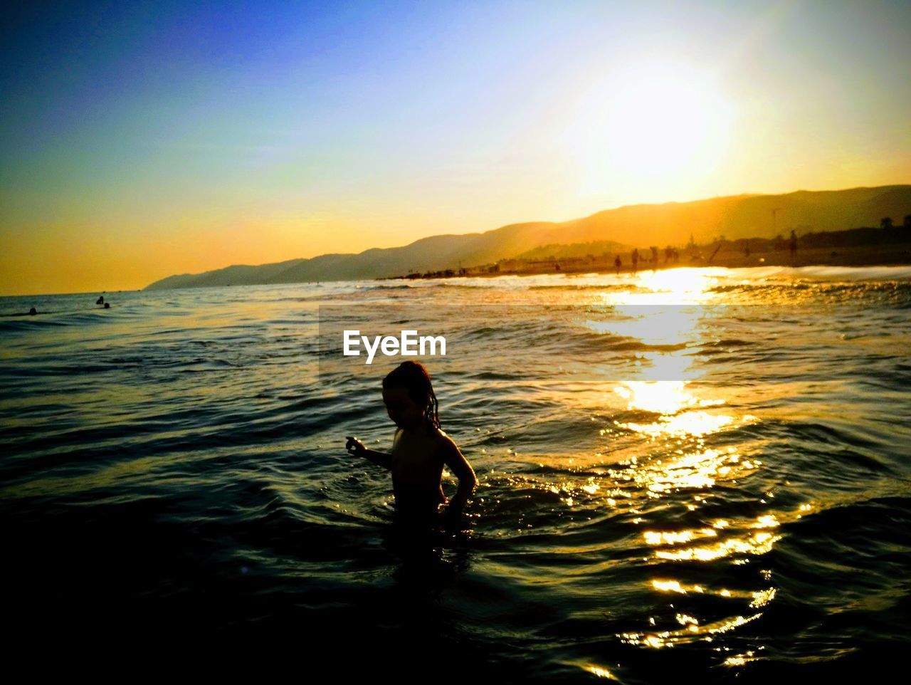 Girl in sea against sky during sunset