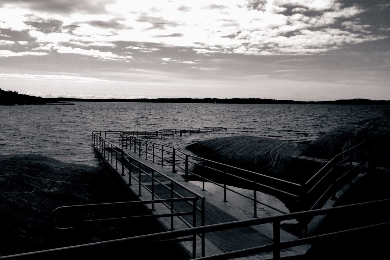 Walkway at lake against cloudy sky