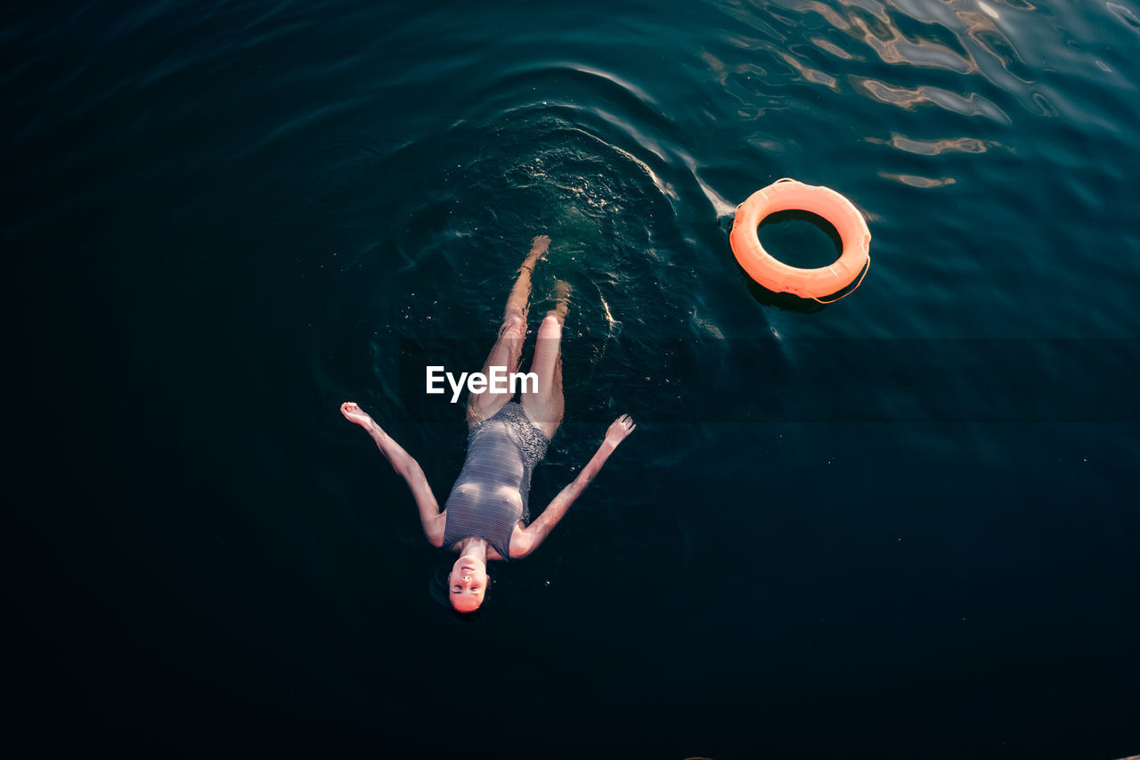 HIGH ANGLE VIEW OF YOUNG WOMAN SWIMMING IN SEA