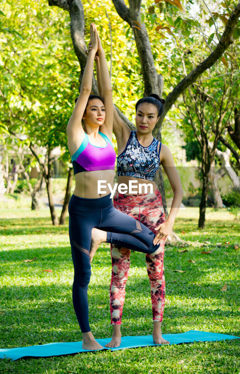 Yoga instructor assisting woman while exercising at park