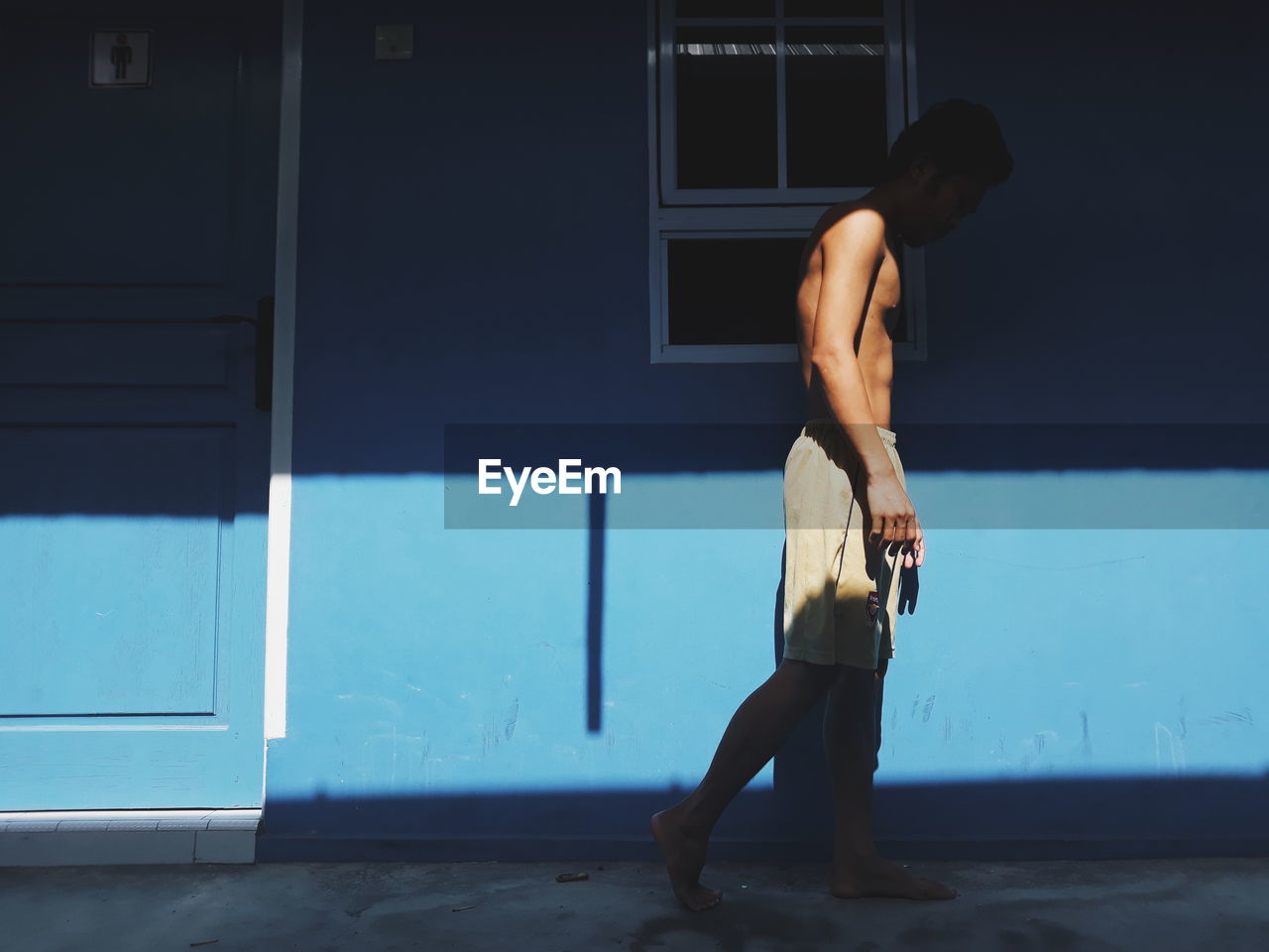 Rear view of shirtless man standing in blue house