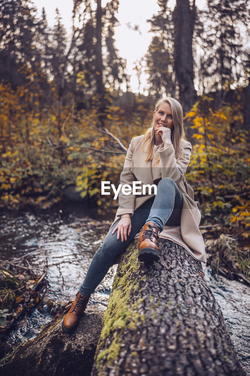 tree, autumn, forest, adult, women, nature, plant, one person, leisure activity, land, young adult, clothing, blond hair, lifestyles, sitting, beauty in nature, portrait photography, full length, spring, plant part, hairstyle, emotion, leaf, smiling, outdoors, woodland, happiness, relaxation, female, long hair, casual clothing, tranquility, sunlight, day, activity, footwear, landscape, portrait, looking, holiday, person, sky, photo shoot, environment, trip, vacation, fashion, dress, tree trunk, rural scene