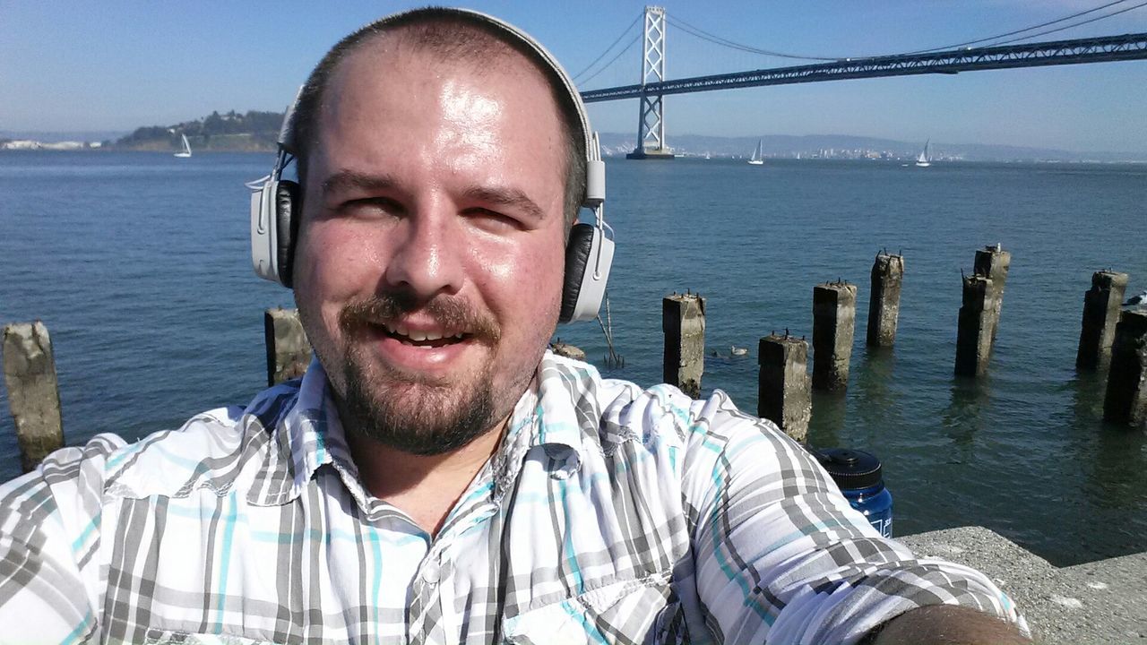 Portrait of man listening to music through headphones against bridge over sea