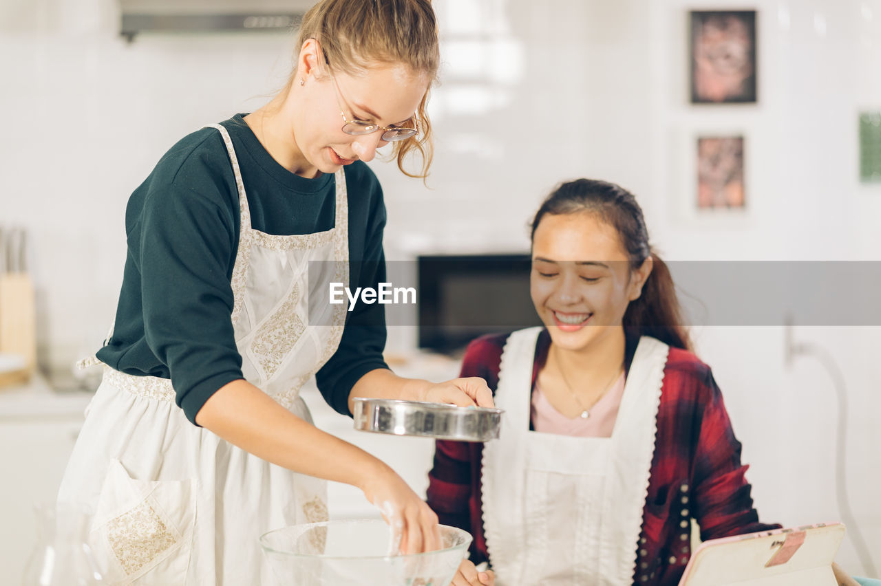 Two women make on a cake in kitchen
