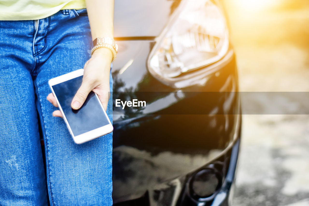 Midsection of woman holding mobile phone by car