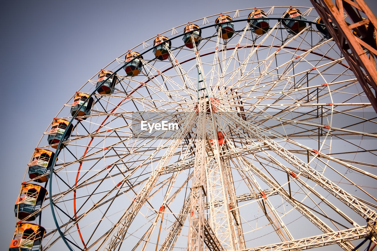 ferris wheel, amusement park ride, amusement park, arts culture and entertainment, carnival, traveling carnival, sky, fun, nature, leisure activity, low angle view, circle, no people, geometric shape, architecture, travel destinations, enjoyment, shape, outdoors, large, clear sky, recreation, amber, spinning, built structure, day, turning, amusement ride, grey, blue
