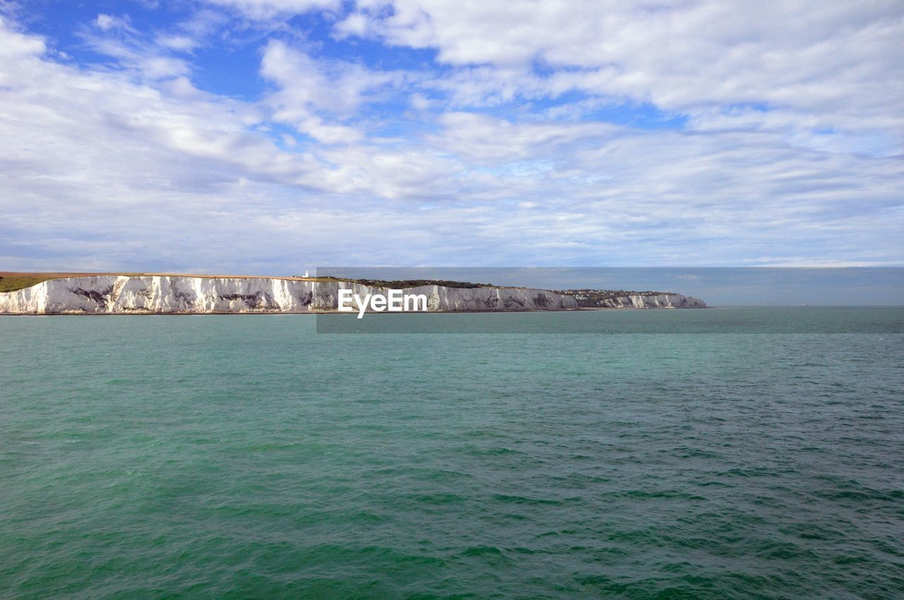 Scenic view of sea by white cliffs of dover against cloudy sky