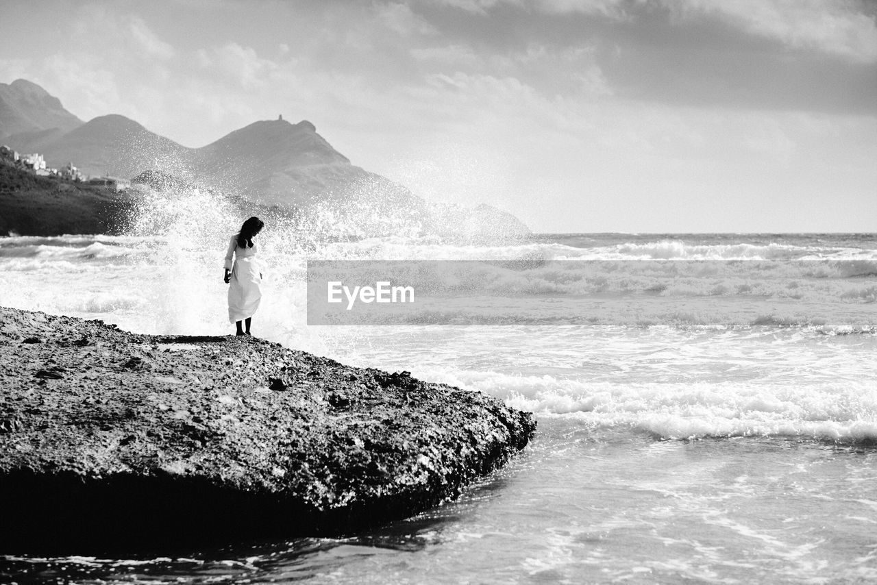 Woman standing on rock by sea against sky