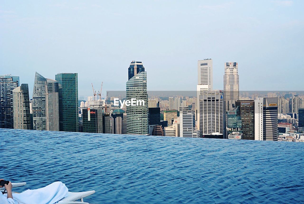 Low section of man resting by swimming pool at marina bay sands against city