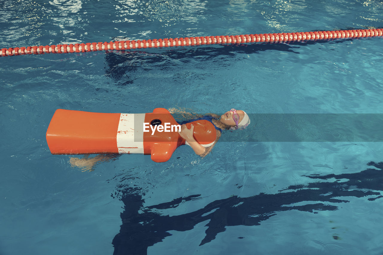 High angle view of girl swimming with dummy in pool