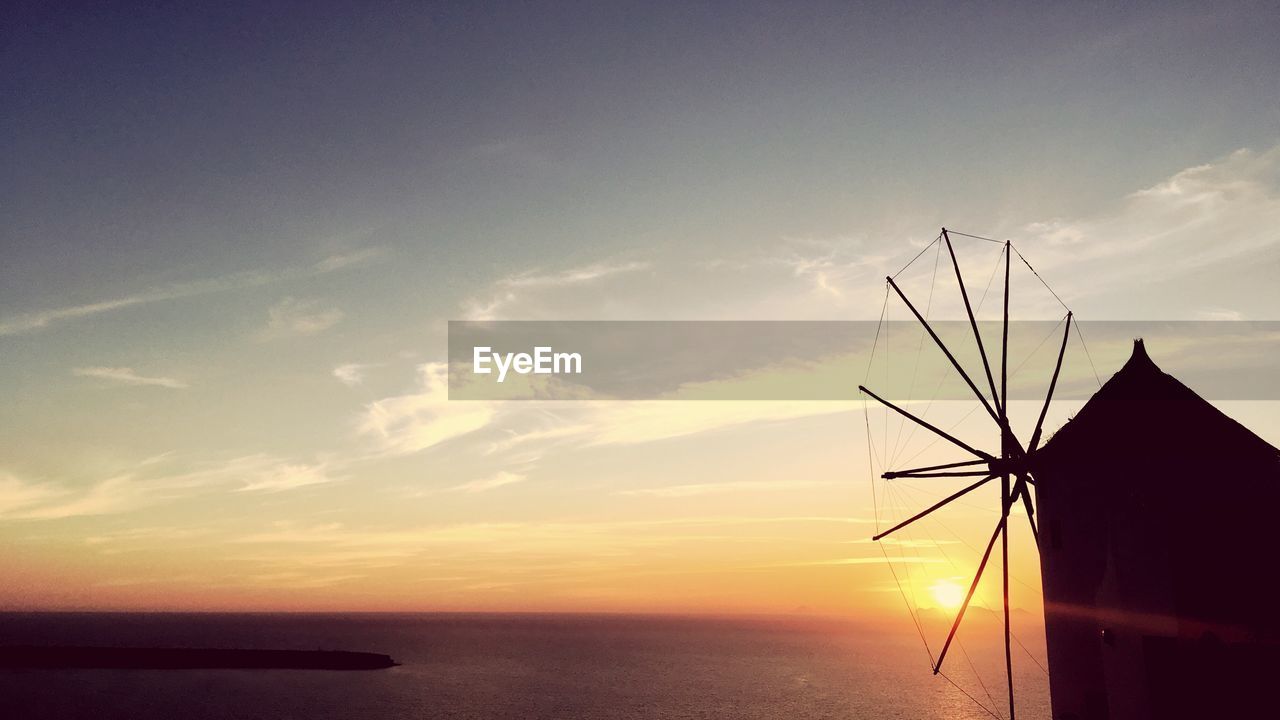Silhouette of traditional windmill by sea against sky