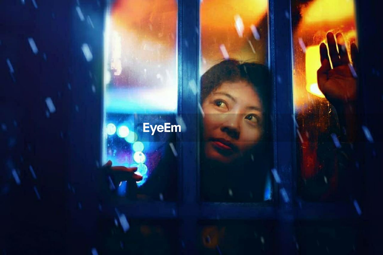 Portrait of woman looking through window at night