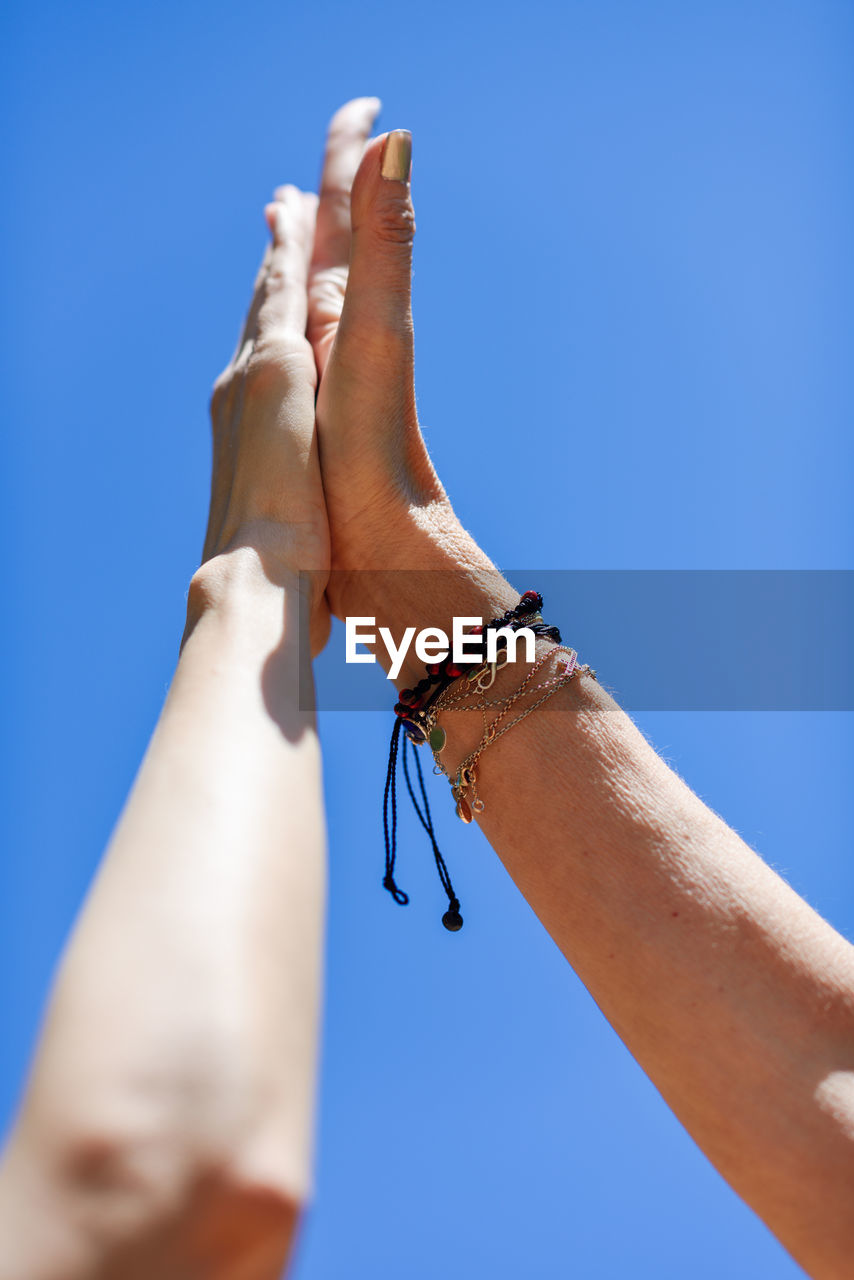 Low angle view of cropped hands giving high-five against clear blue sky