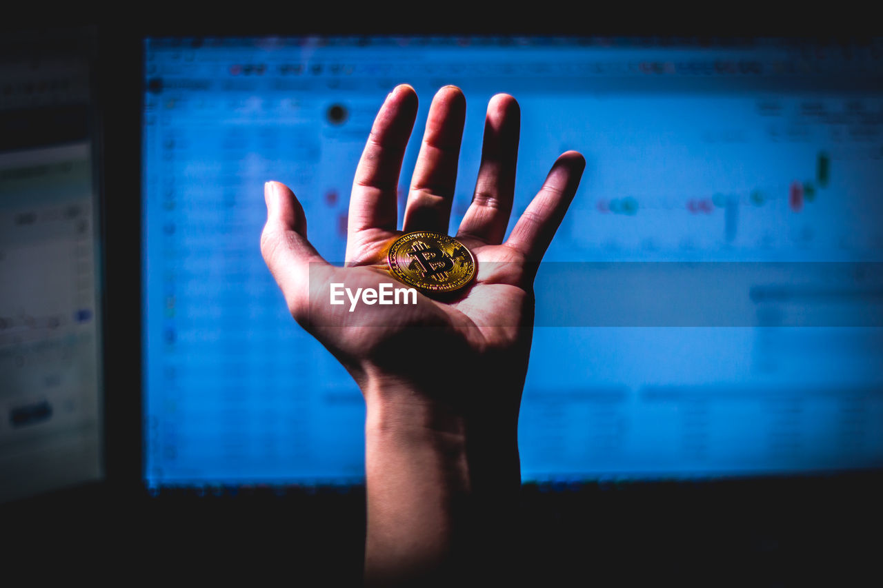 Cropped hand of woman holding bitcoin against computer