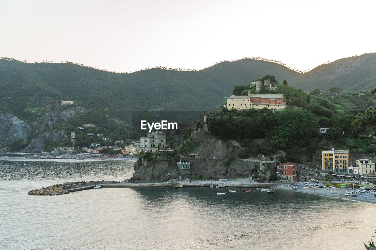 Picturesque drone view of houses and beach of resort town located near sea against green mountains and sundown sky