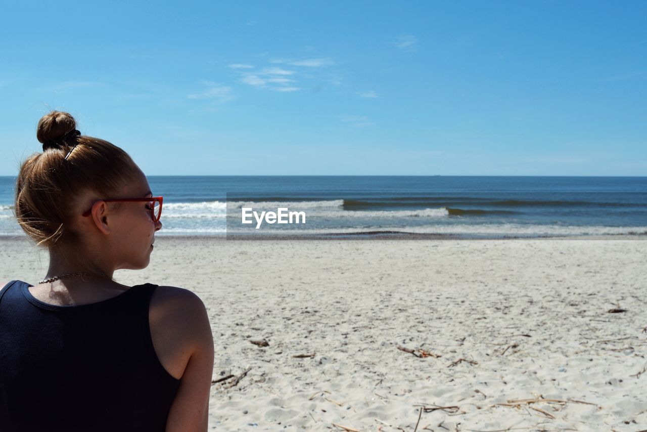 Rear view of young woman resting on beach against sky