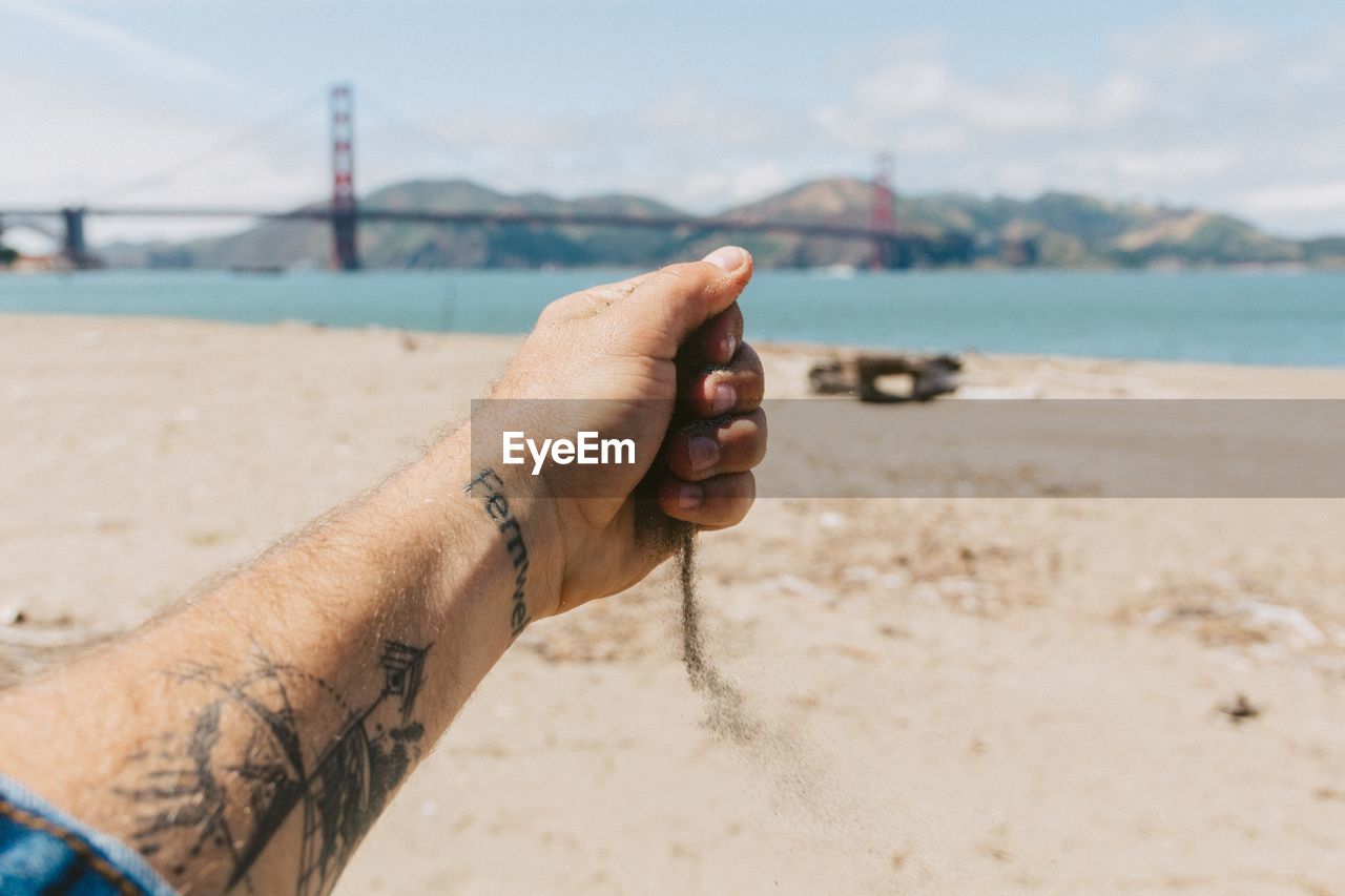 Cropped image of hand holding sand with golden gate bridge in background
