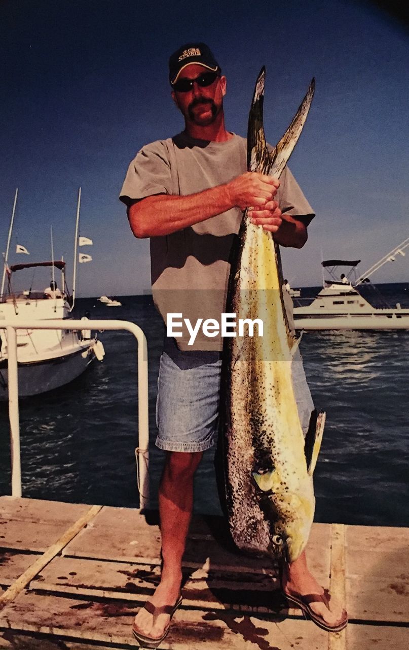 Full length of man holding fish by sea against sky