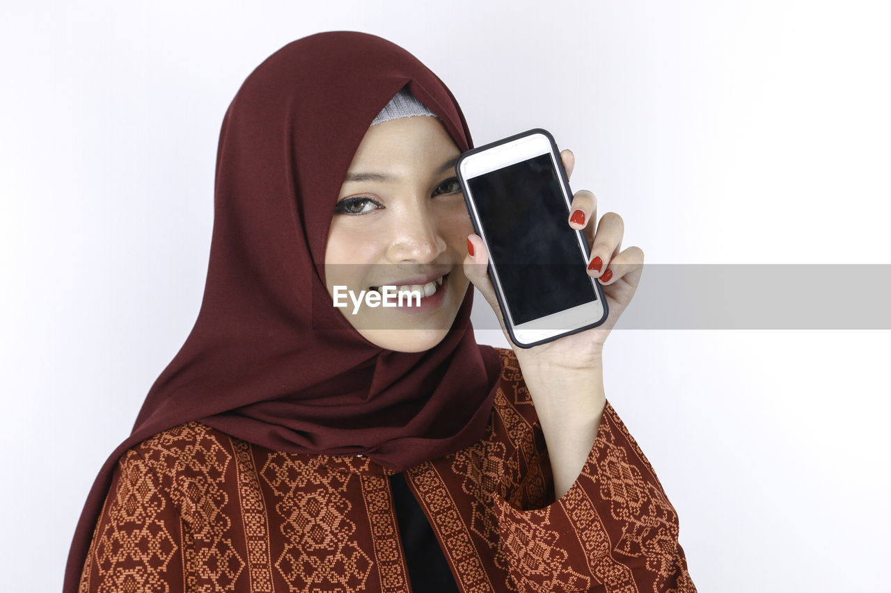 PORTRAIT OF SMILING YOUNG WOMAN USING MOBILE PHONE
