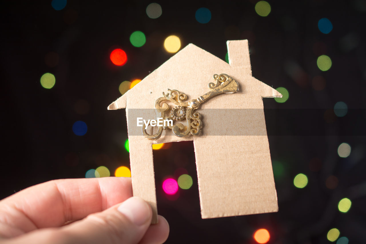 Close-up of human hand holding cardboard model home against colorful lens flares