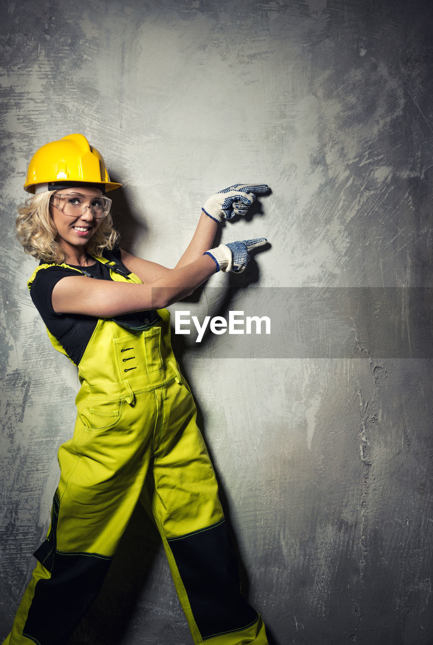 Portrait of smiling female worker pointing at concrete wall