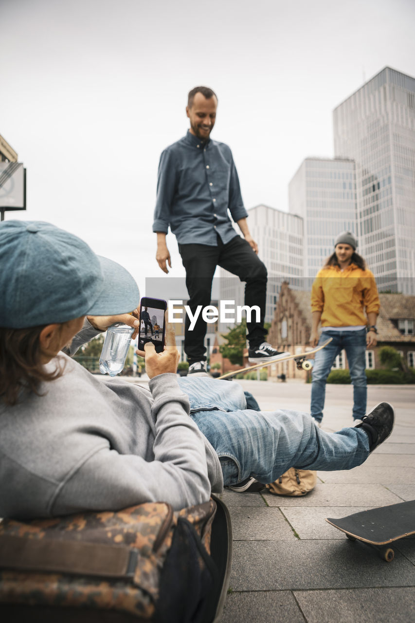 Man photographing while male friend skating on footpath