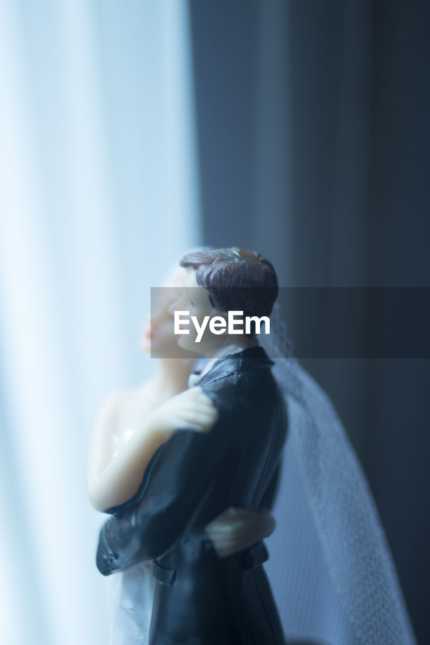 Close-up of wedding cake figurine on table by window at home