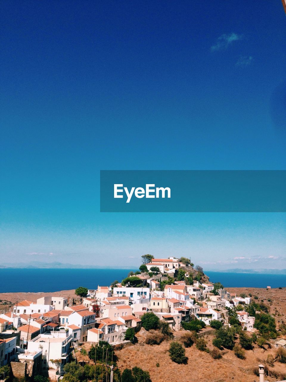 High angle view of houses by sea against clear blue sky