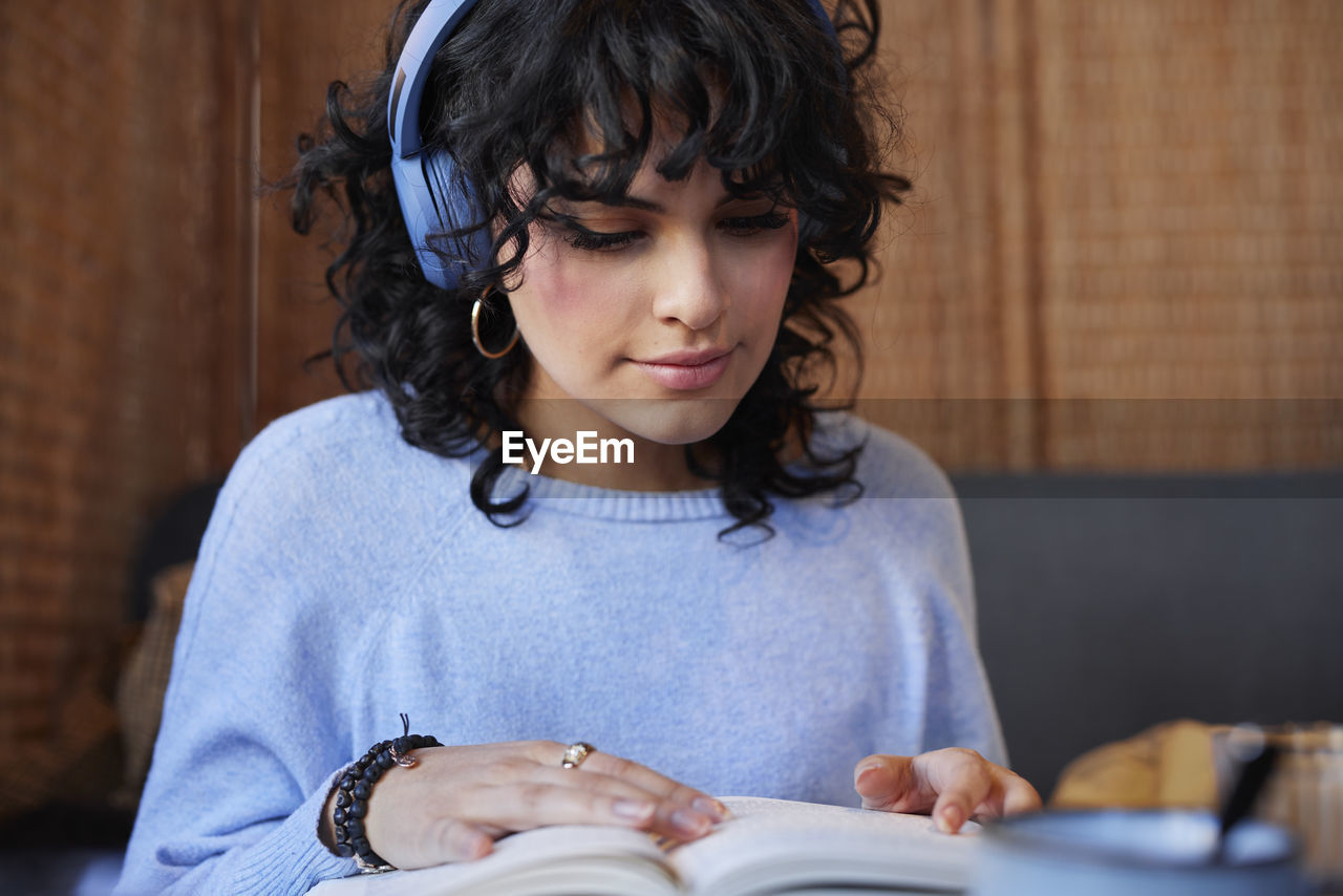 Young woman in headphones reading book while studying