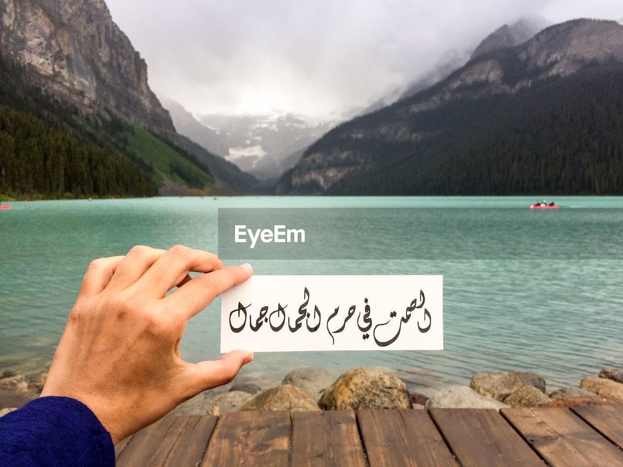 Cropped hand holding text against lake and mountains