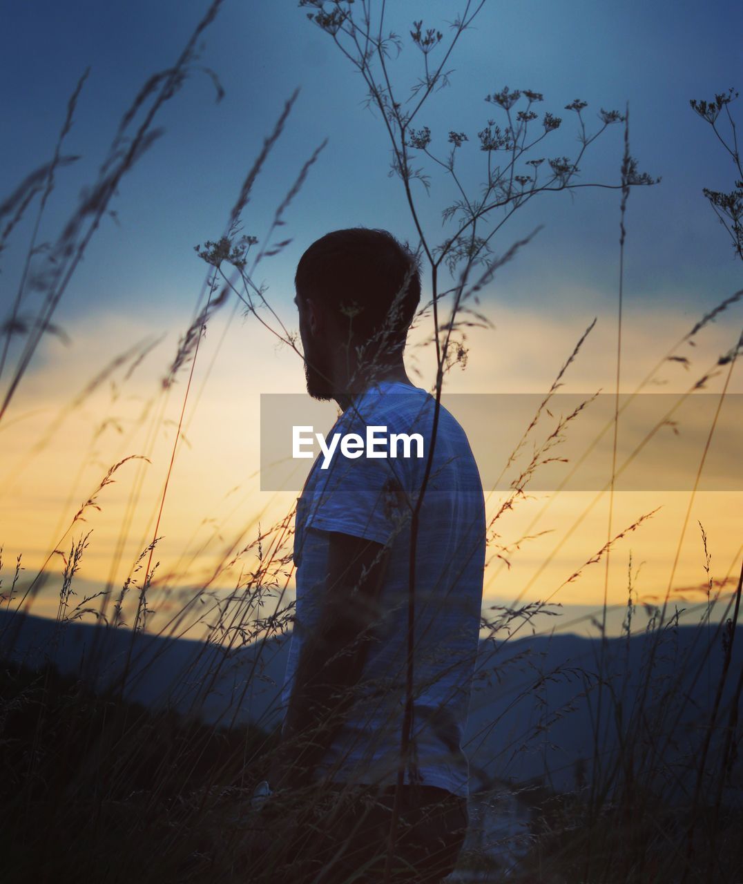 Side view of man standing against sky at sunset