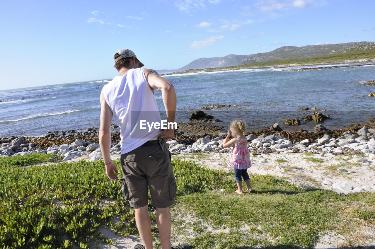 Rear view of father scratching by daughter standing by sea