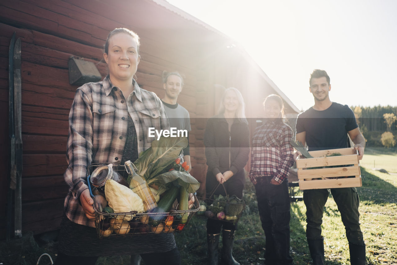 Portrait of smiling farmers carrying organic vegetables outside barn