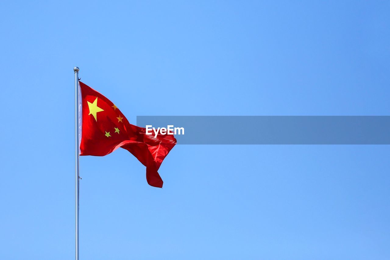 Low angle view of chinese flag against clear blue sky