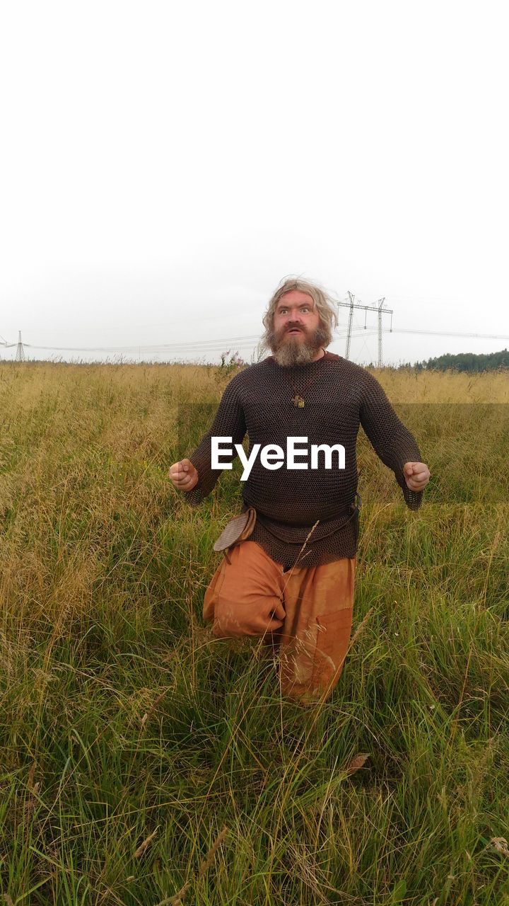 MAN WITH ARMS RAISED ON FIELD AGAINST SKY