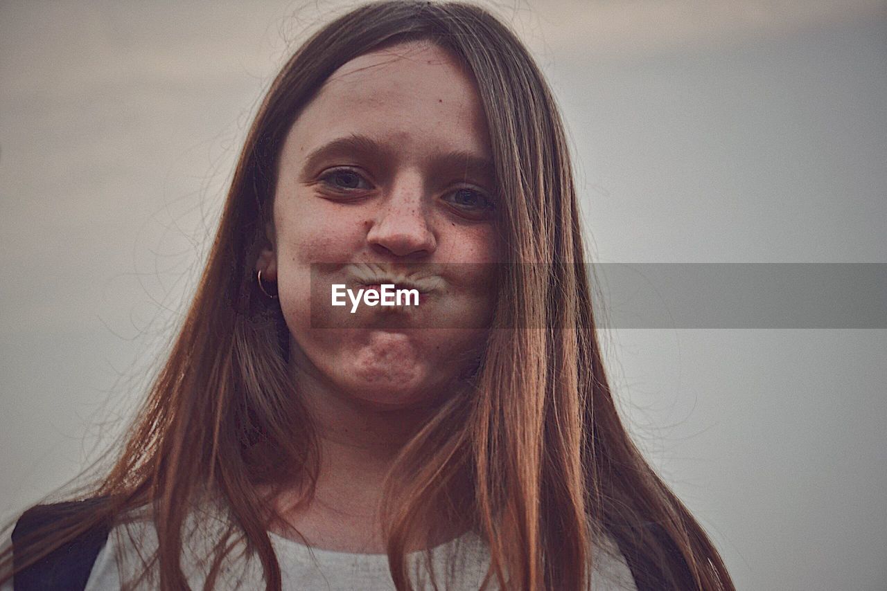 Portrait of smiling young woman making a face against sky