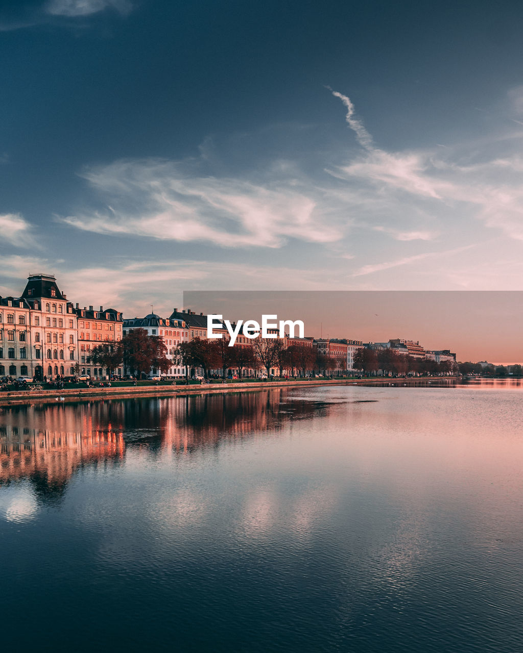 Scenic view of river by buildings against sky during sunset