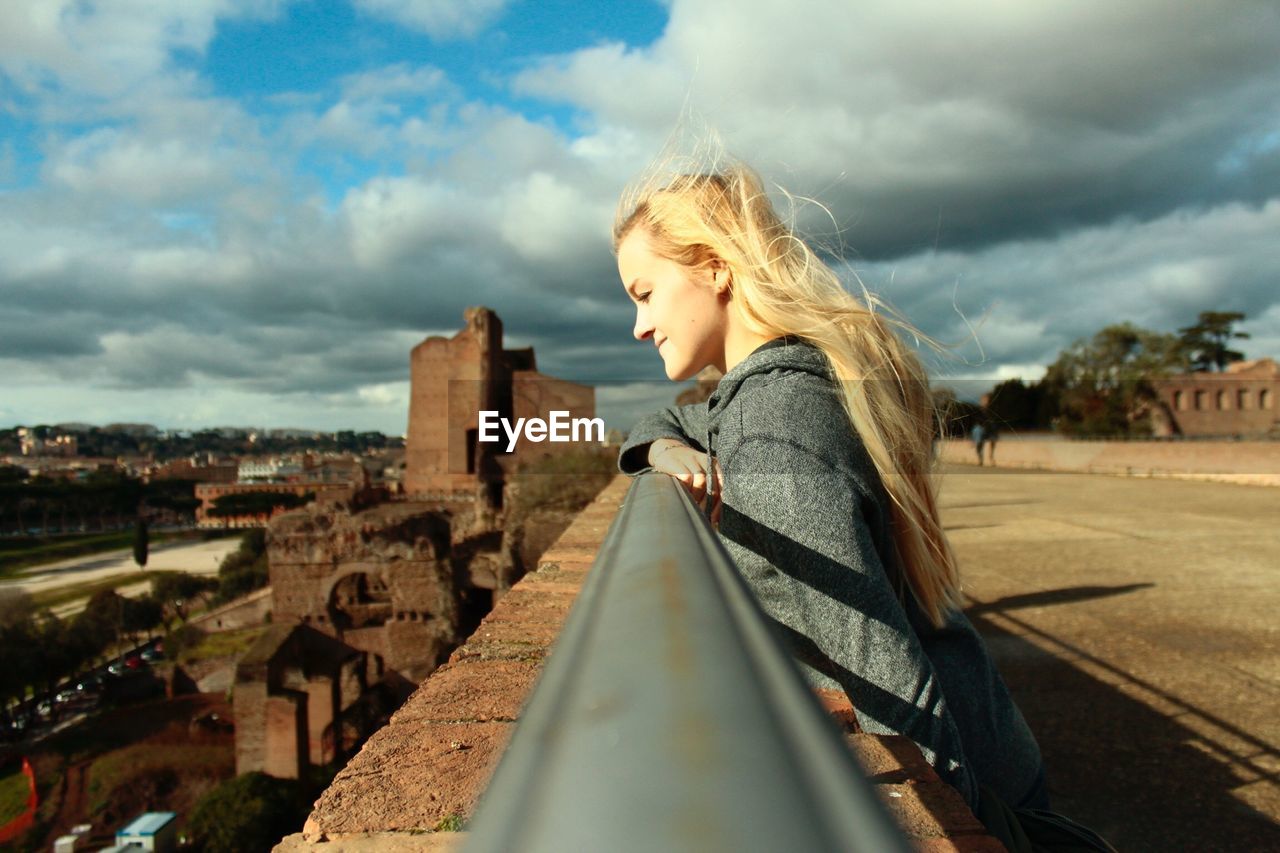 Side view of smiling young woman standing on bridge