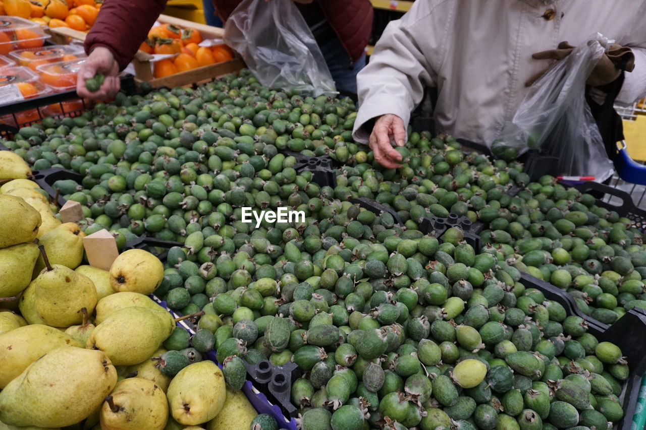 Hands of people choosing fruits in a supermarket. heap of feijoa, for sale